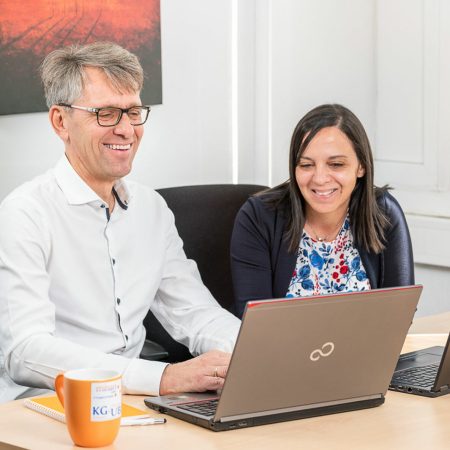 imagebild mitarbeiter am laptop neben ihm sitzt seine kollegin beide haben spass an der arbeit